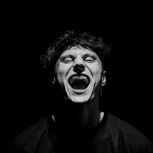 Fantasm, artiste techno, en portrait noir et blanc, hurlant avec énergie sur un fond sombre.